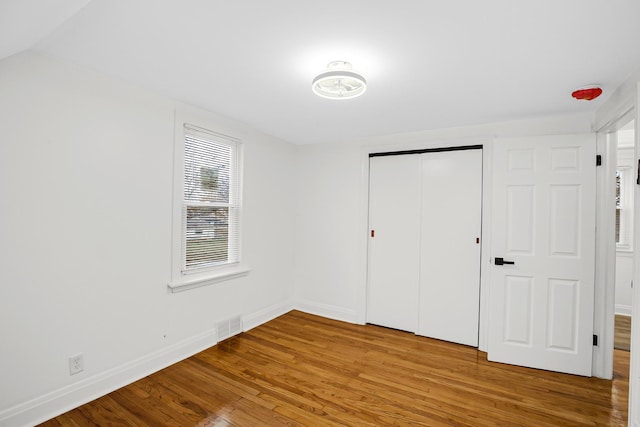 unfurnished bedroom with wood-type flooring, vaulted ceiling, and a closet