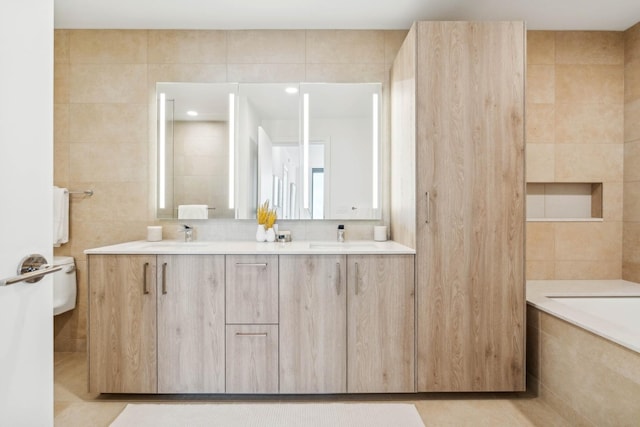 bathroom with tile patterned floors, tiled tub, toilet, vanity, and tile walls