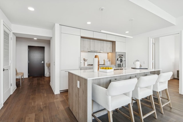 kitchen with a breakfast bar, dark wood-type flooring, a center island with sink, sink, and hanging light fixtures