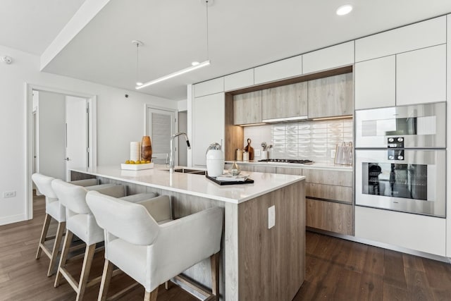 kitchen featuring a breakfast bar area, a kitchen island with sink, sink, and dark hardwood / wood-style floors