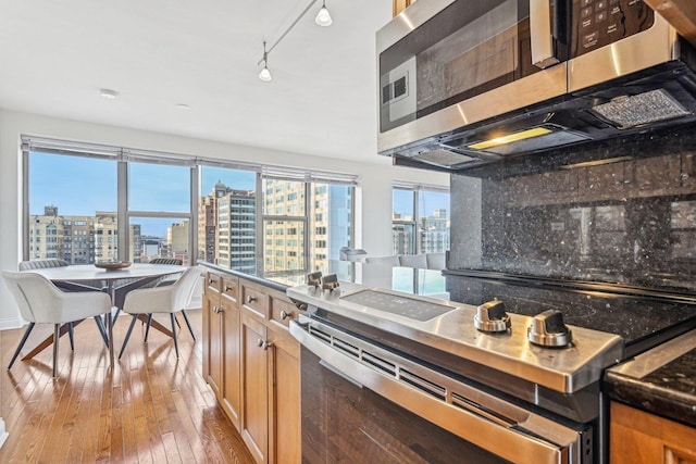 kitchen with appliances with stainless steel finishes, light hardwood / wood-style floors, track lighting, and tasteful backsplash