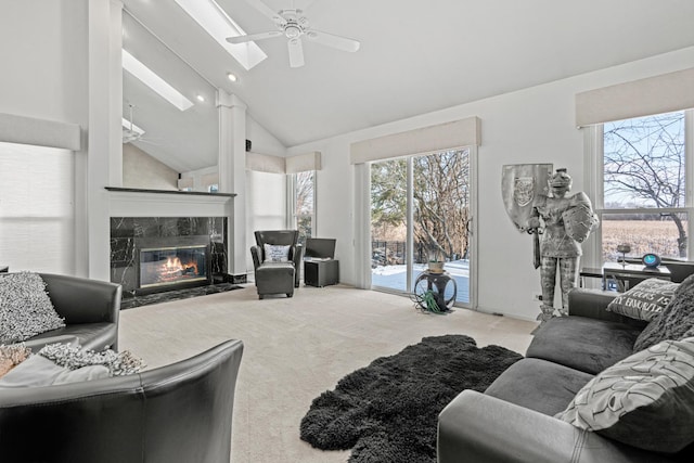 carpeted living room with a high end fireplace, a skylight, high vaulted ceiling, and ceiling fan