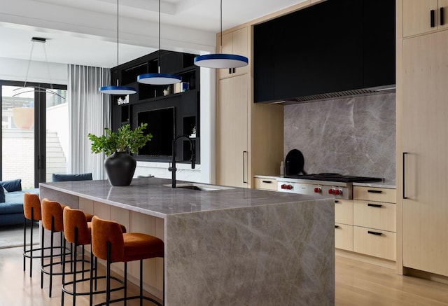 kitchen with sink, a breakfast bar area, hanging light fixtures, a kitchen island with sink, and exhaust hood