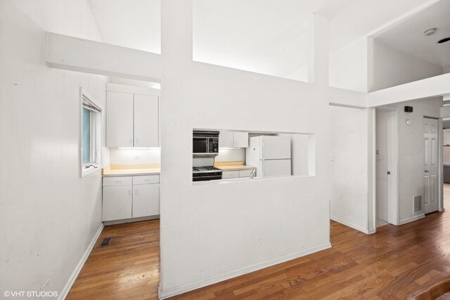 kitchen with white cabinetry, hardwood / wood-style floors, a towering ceiling, white fridge, and stainless steel range with gas stovetop