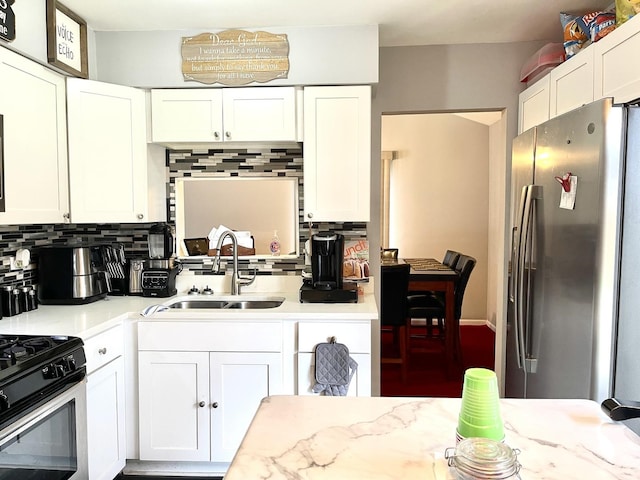 kitchen with white cabinets, black range with gas stovetop, sink, decorative backsplash, and stainless steel fridge