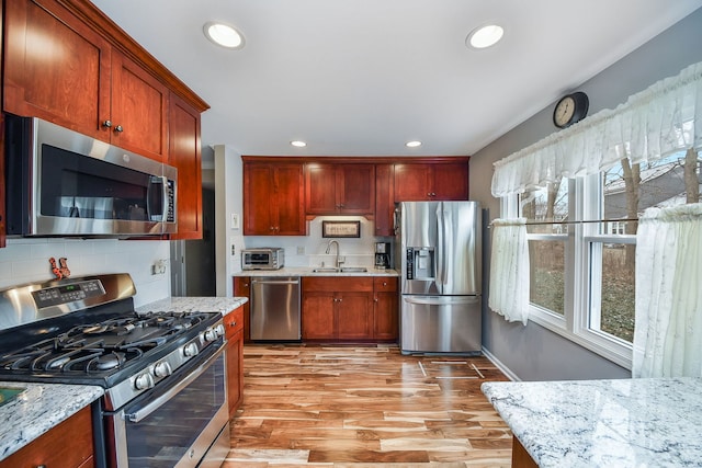 kitchen with light stone counters, stainless steel appliances, sink, and light hardwood / wood-style flooring