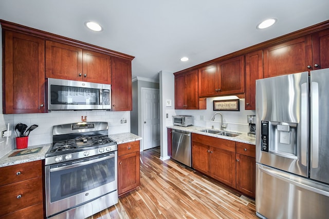 kitchen featuring appliances with stainless steel finishes, sink, backsplash, light stone countertops, and light wood-type flooring