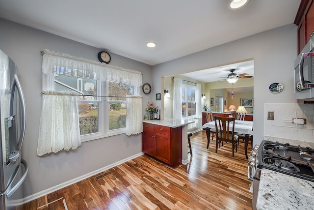 kitchen featuring hardwood / wood-style floors, tasteful backsplash, ceiling fan, light stone counters, and stainless steel appliances