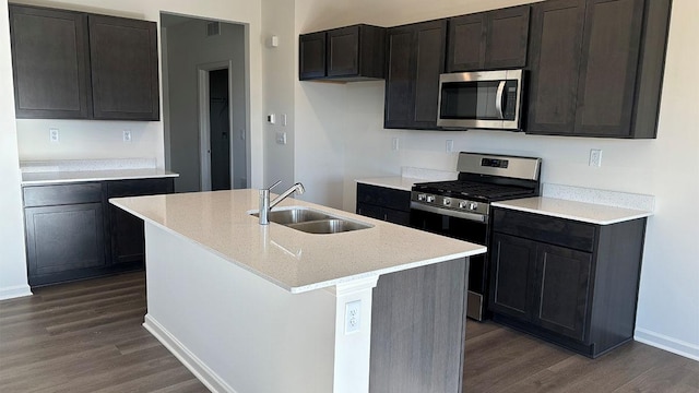 kitchen with appliances with stainless steel finishes, a kitchen island with sink, sink, and dark hardwood / wood-style floors