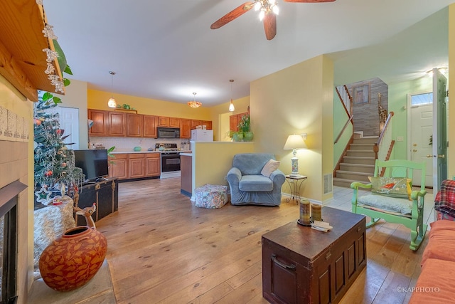 living room with a tile fireplace, ceiling fan, and light hardwood / wood-style floors