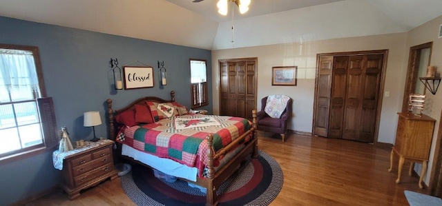 bedroom with ceiling fan, multiple closets, wood-type flooring, and vaulted ceiling