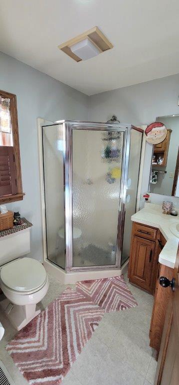 bathroom featuring tile patterned flooring, vanity, toilet, and a shower with shower door