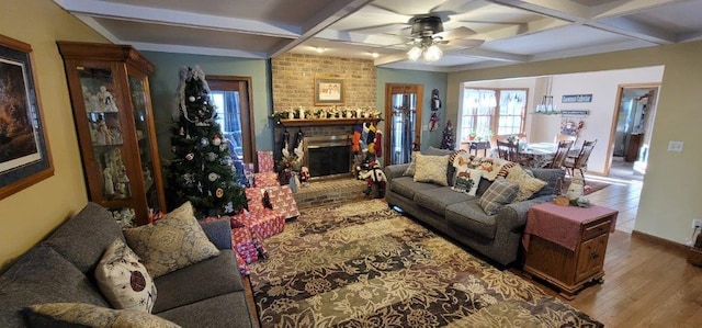 living room with ceiling fan, coffered ceiling, a brick fireplace, beamed ceiling, and light wood-type flooring