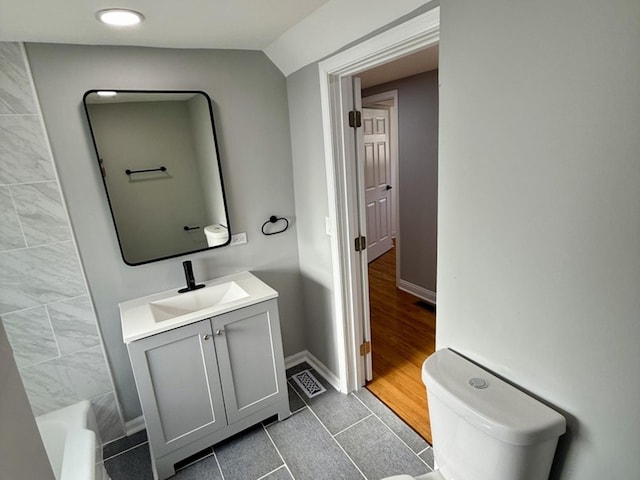 bathroom featuring wood-type flooring, lofted ceiling, toilet, a bathtub, and vanity