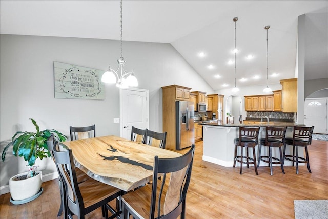 dining space featuring a notable chandelier, light hardwood / wood-style floors, sink, and high vaulted ceiling