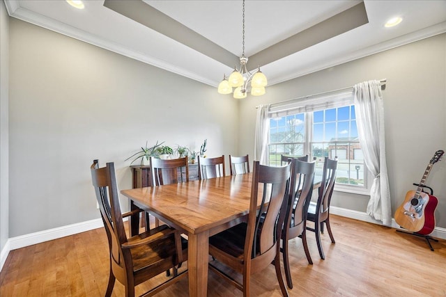 dining space with a raised ceiling, light hardwood / wood-style flooring, ornamental molding, and an inviting chandelier