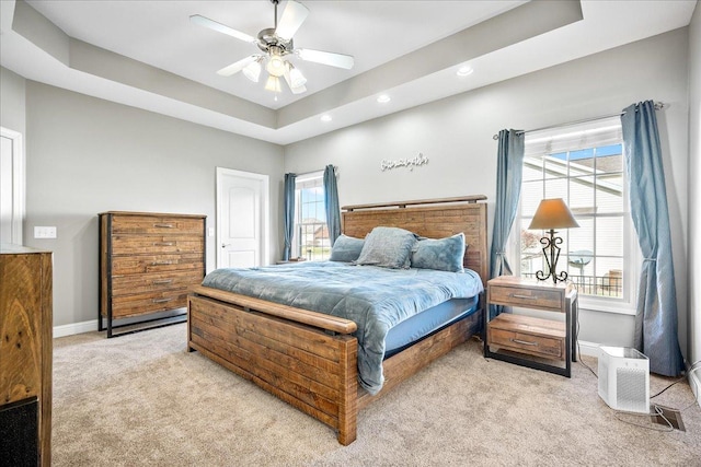 bedroom featuring a raised ceiling, ceiling fan, and light colored carpet