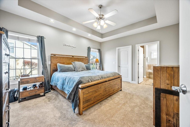 bedroom with a raised ceiling, connected bathroom, ceiling fan, and light carpet