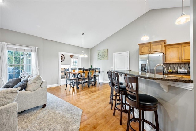 kitchen featuring pendant lighting, decorative backsplash, stainless steel fridge with ice dispenser, and a breakfast bar area