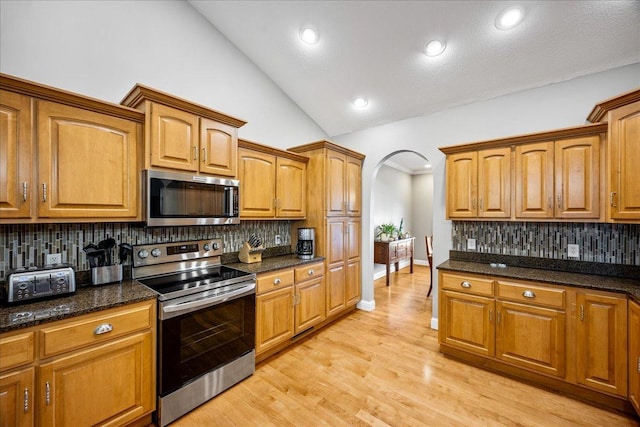 kitchen featuring decorative backsplash, appliances with stainless steel finishes, vaulted ceiling, and dark stone countertops