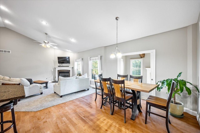 dining space with ceiling fan with notable chandelier, light hardwood / wood-style floors, and vaulted ceiling