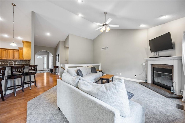 living room featuring ceiling fan, sink, high vaulted ceiling, and light wood-type flooring