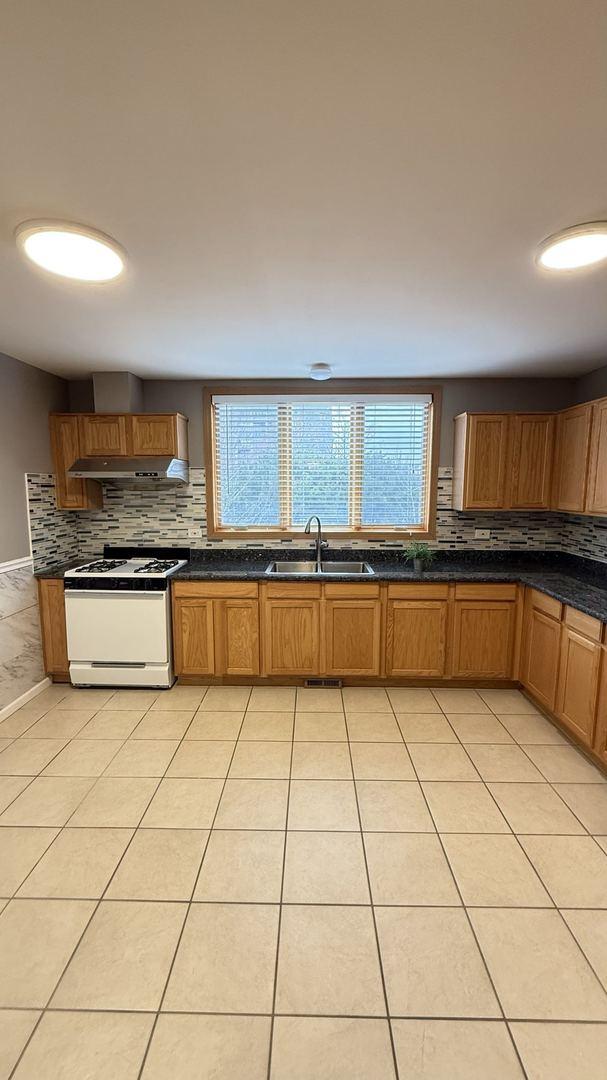 kitchen with white range with gas stovetop, sink, light tile patterned floors, and tasteful backsplash