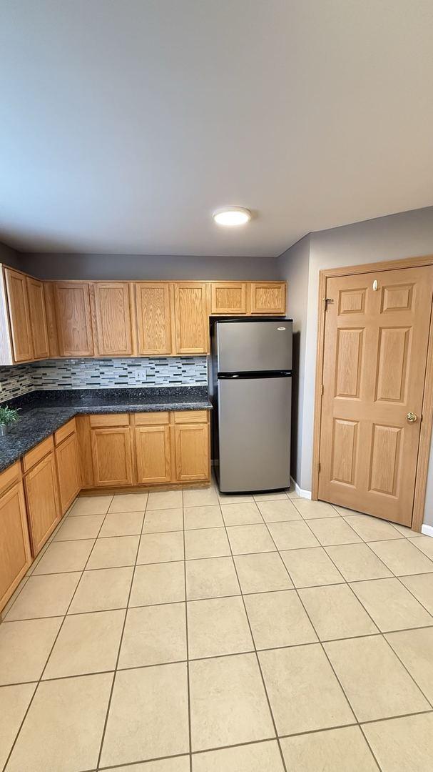 kitchen with stainless steel fridge, light tile patterned floors, and backsplash