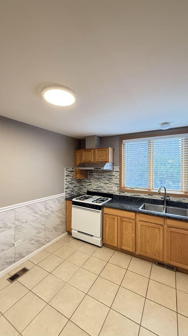 kitchen with white range oven, light tile patterned floors, sink, and tasteful backsplash