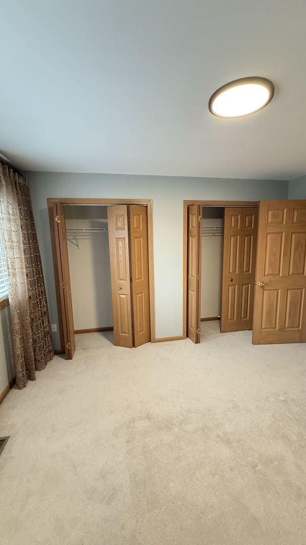 unfurnished bedroom with multiple closets and light carpet