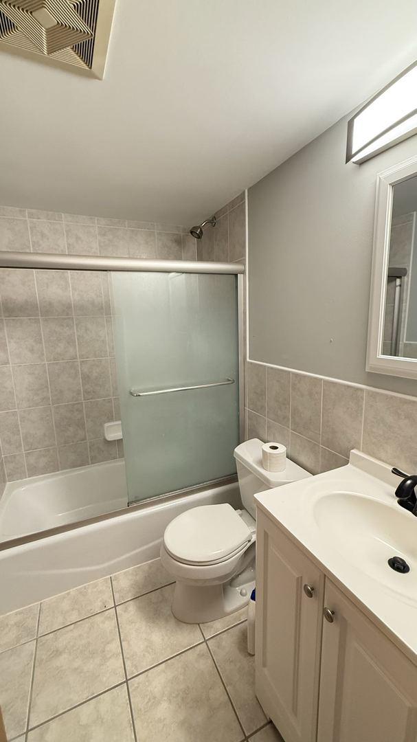 full bathroom featuring tile patterned floors, vanity, tile walls, enclosed tub / shower combo, and toilet