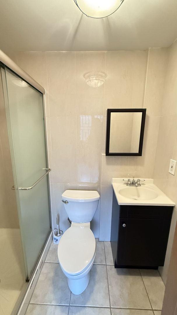 bathroom with vanity, tile walls, tile patterned flooring, toilet, and a shower with shower door