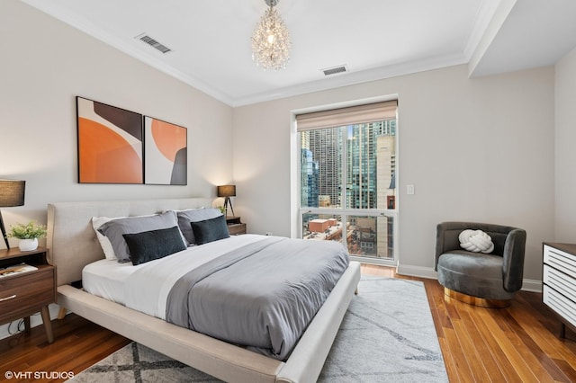 bedroom featuring visible vents, an inviting chandelier, ornamental molding, wood finished floors, and baseboards