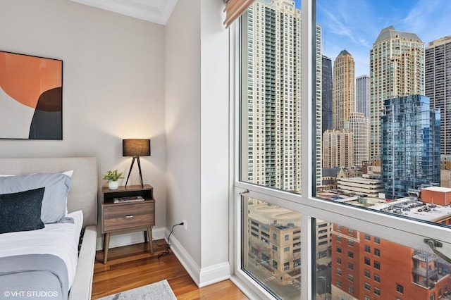 bedroom with ornamental molding, a city view, baseboards, and wood finished floors