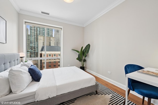 bedroom with ornamental molding, wood finished floors, visible vents, and baseboards