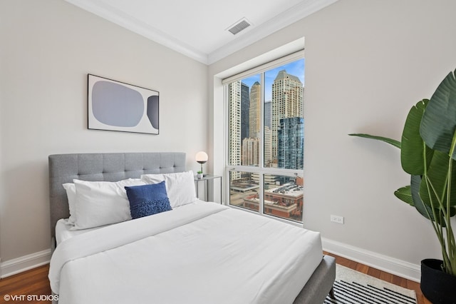 bedroom featuring a city view, wood finished floors, visible vents, baseboards, and ornamental molding