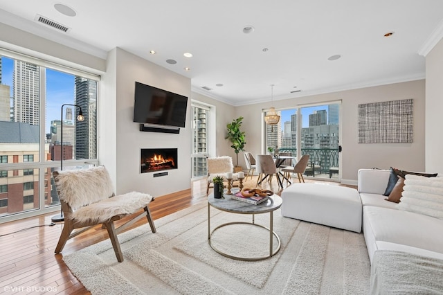 living room with a lit fireplace, ornamental molding, wood finished floors, and visible vents