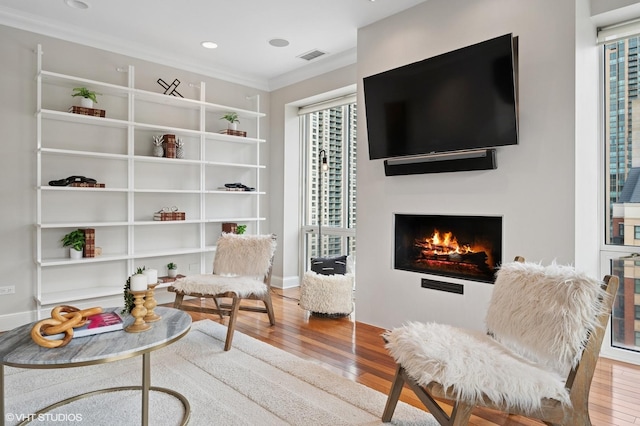 sitting room featuring a lit fireplace, hardwood / wood-style flooring, visible vents, and crown molding