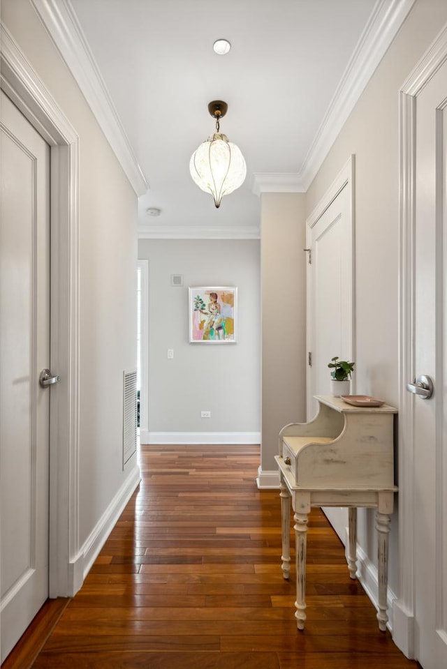 hallway with ornamental molding, wood-type flooring, visible vents, and baseboards