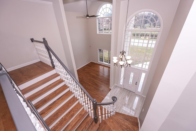 foyer entrance with hardwood / wood-style flooring, ceiling fan with notable chandelier, and a high ceiling