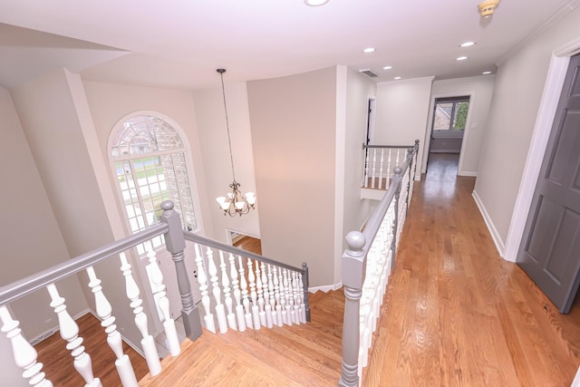 staircase with crown molding, wood-type flooring, and a notable chandelier