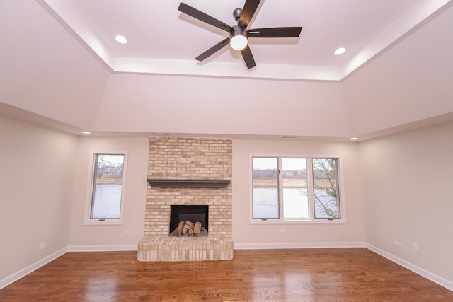 unfurnished living room featuring hardwood / wood-style flooring, ceiling fan, a raised ceiling, and a fireplace