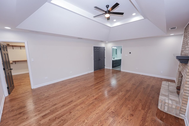 unfurnished living room featuring a fireplace, hardwood / wood-style floors, a tray ceiling, and ceiling fan