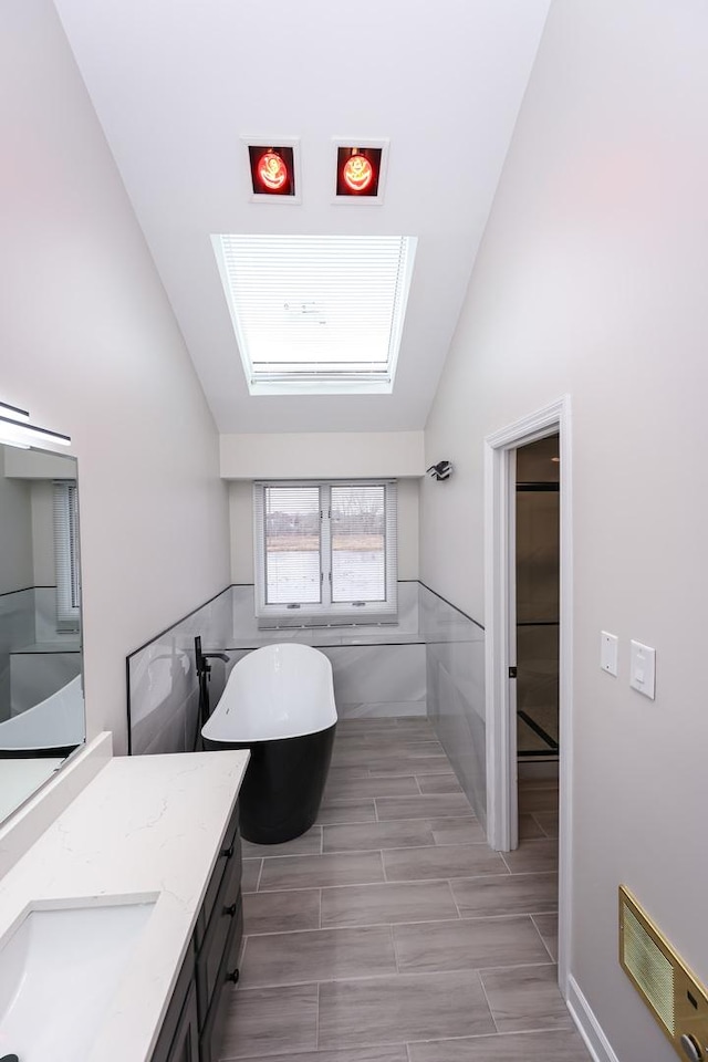 bathroom with vaulted ceiling with skylight, vanity, a tub to relax in, and tile walls