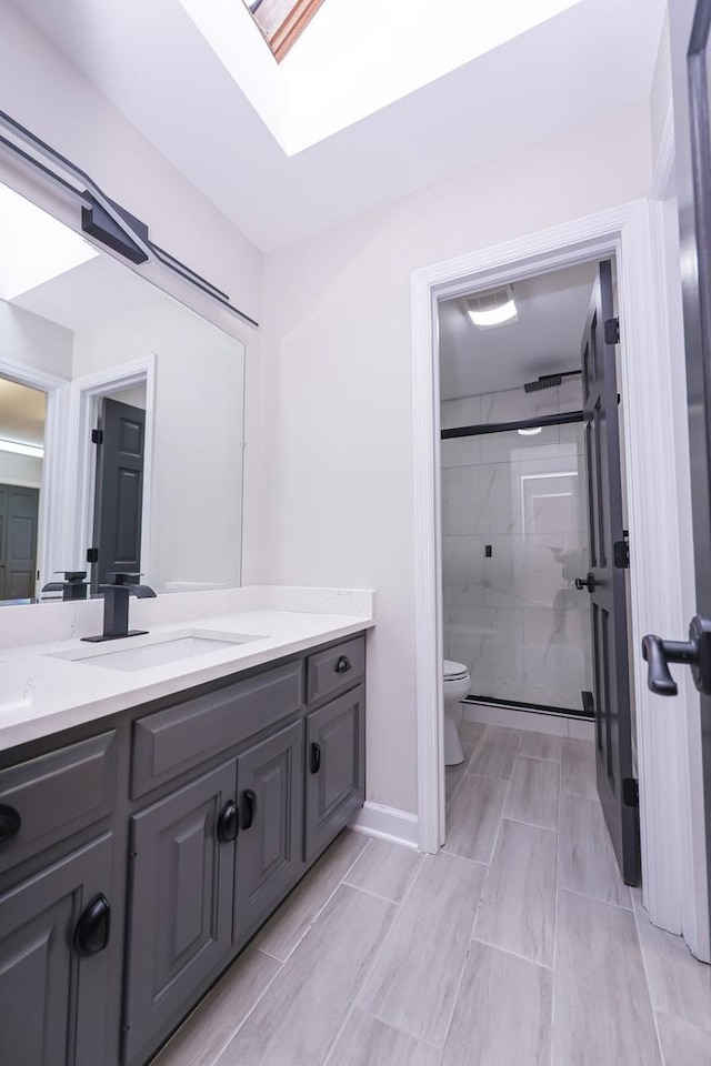 bathroom with a skylight, a shower with door, vanity, and toilet