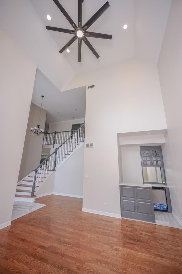 unfurnished living room featuring light hardwood / wood-style flooring, high vaulted ceiling, and ceiling fan with notable chandelier