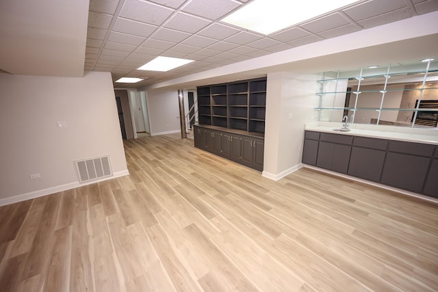 unfurnished living room with light hardwood / wood-style flooring, a drop ceiling, and sink