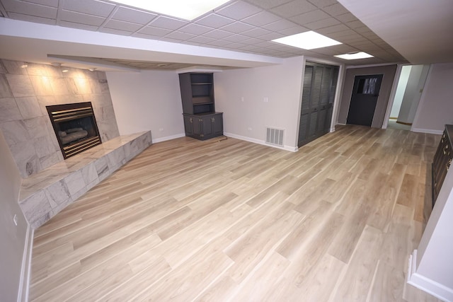 unfurnished living room featuring a tiled fireplace, a paneled ceiling, and light hardwood / wood-style flooring