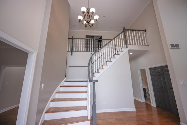 stairway with hardwood / wood-style floors, a towering ceiling, and an inviting chandelier