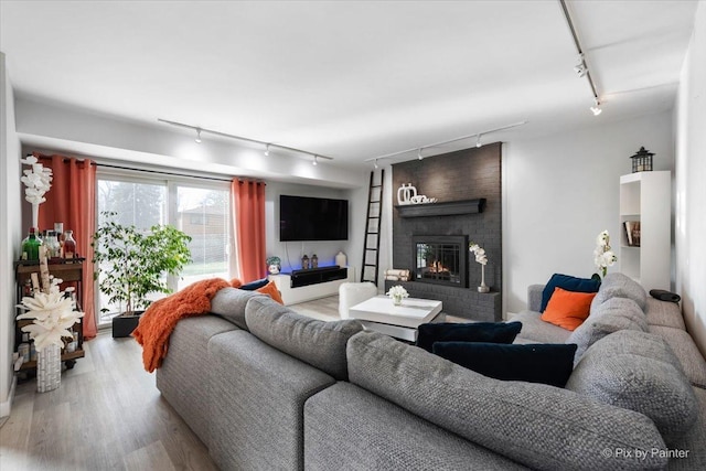 living room featuring light hardwood / wood-style floors, track lighting, and a brick fireplace